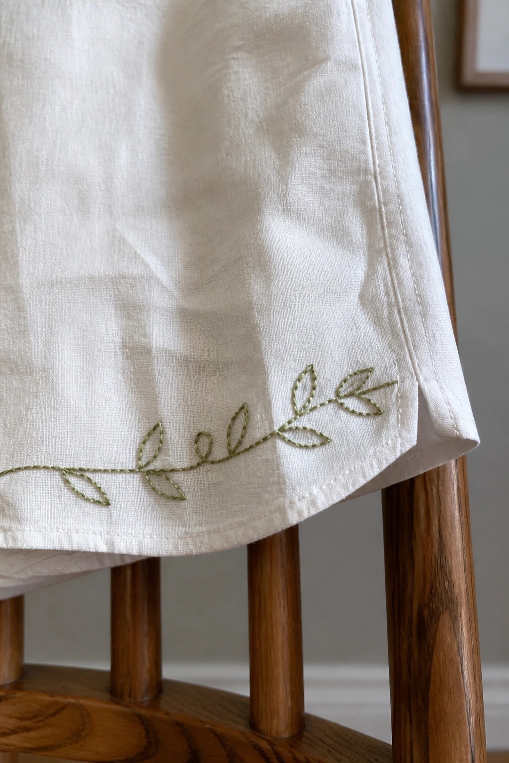 White linen fabric with green embroidered vine draped over wooden chair