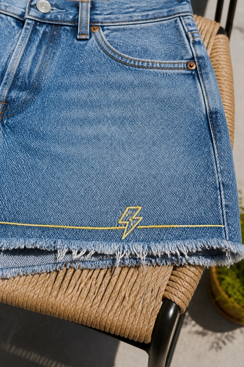 Light blue frayed denim skirt with gold lightning bolt embroidery on woven chair
