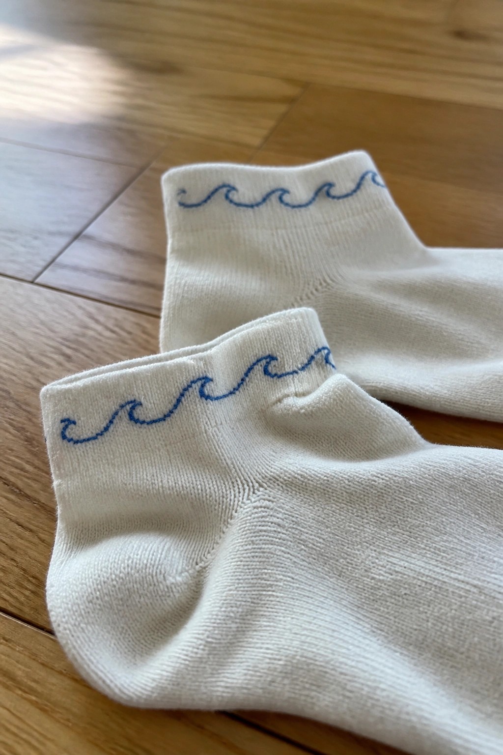 White ankle socks with blue wavy embroidery on wooden floor