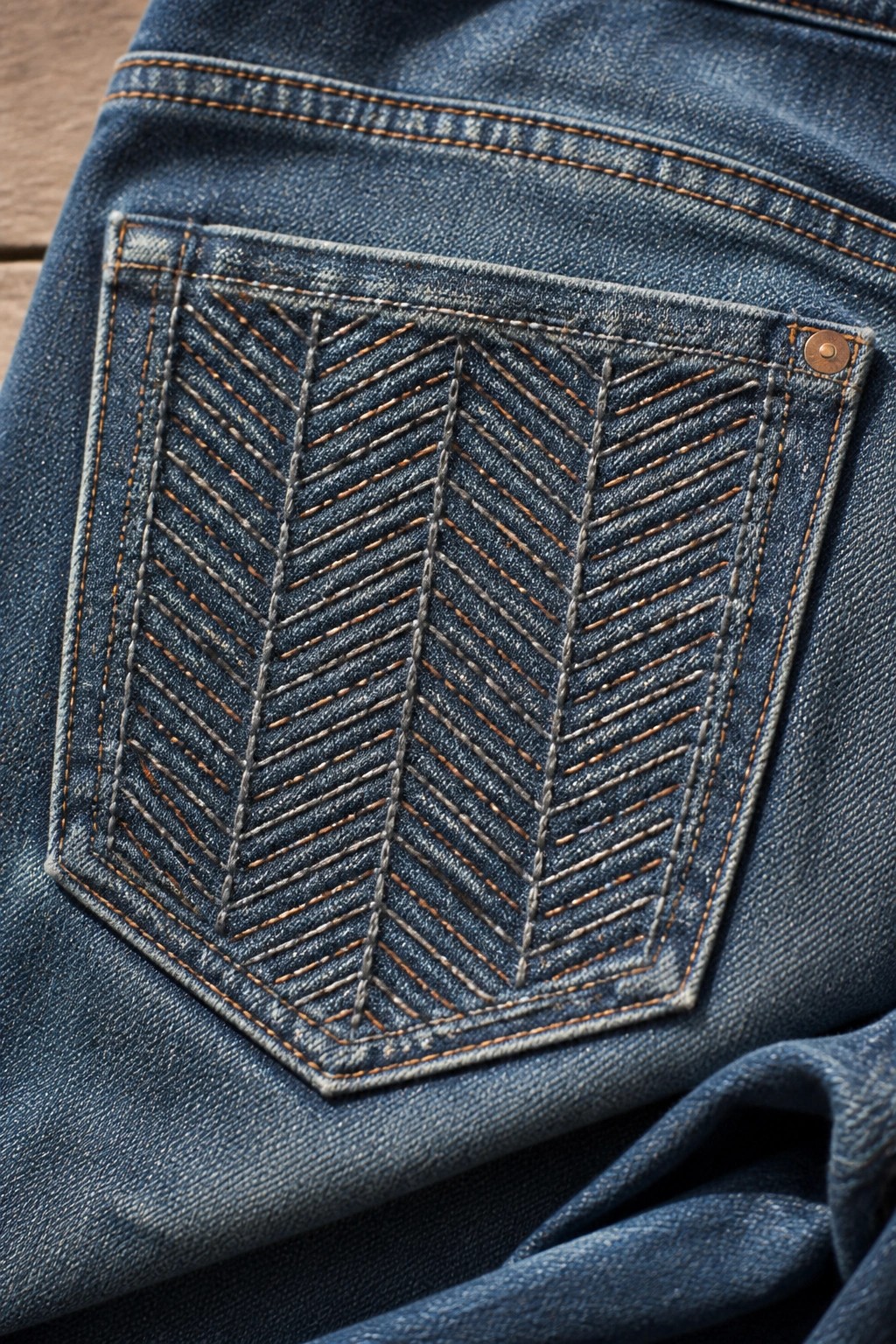 Blue denim jeans pocket with orange herringbone stitching and copper rivet