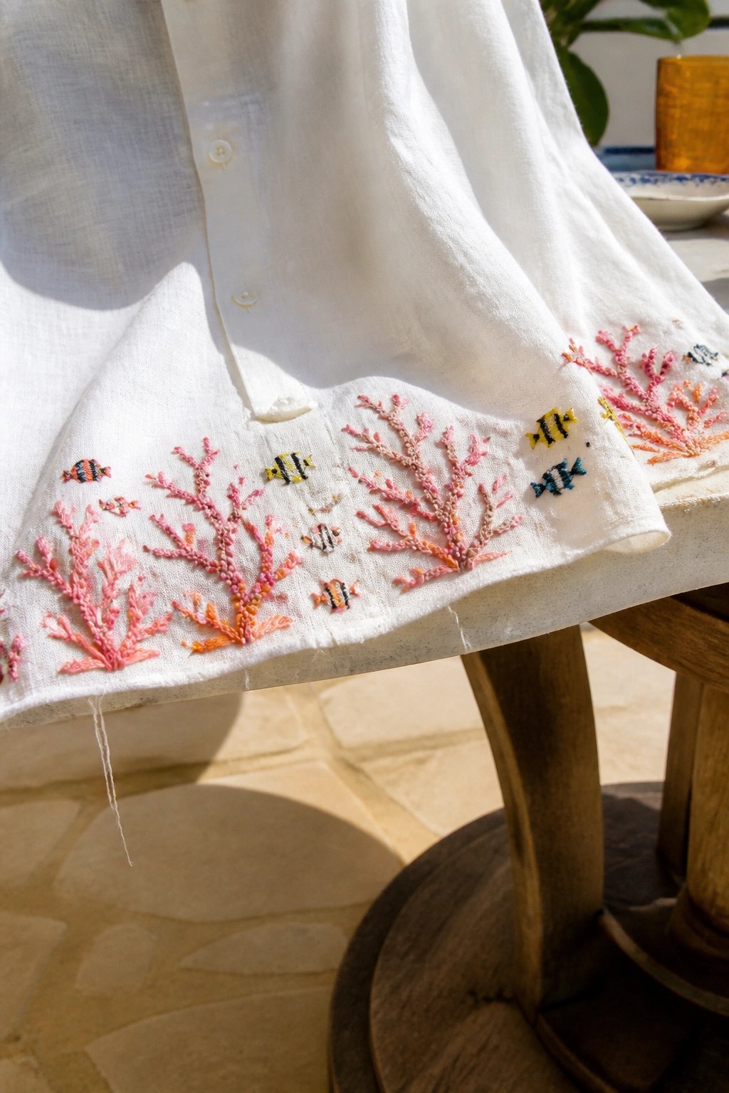 White shirt embroidered with pink coral and striped fish on wooden stool