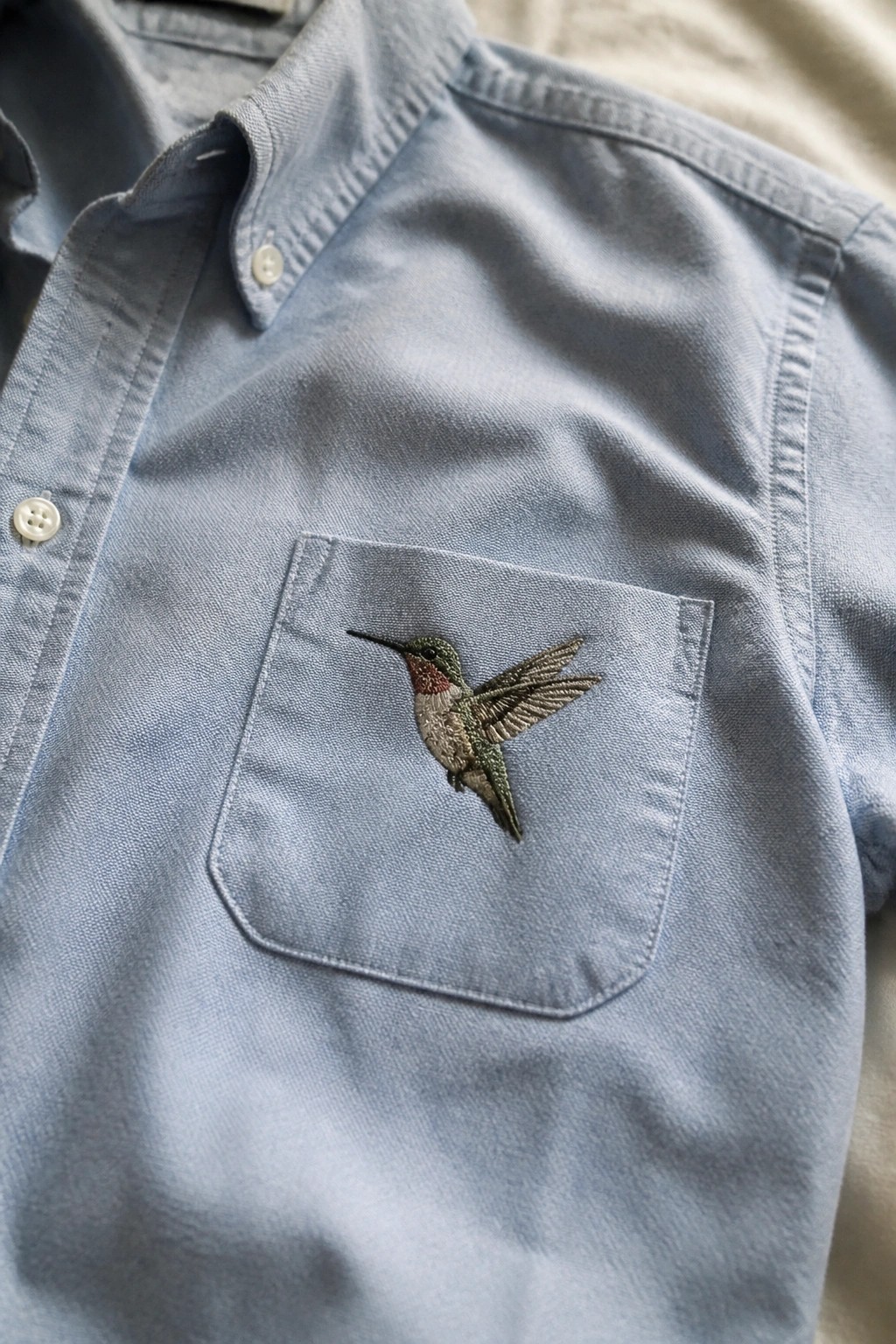 Light blue button-up shirt with embroidered hummingbird on chest pocket