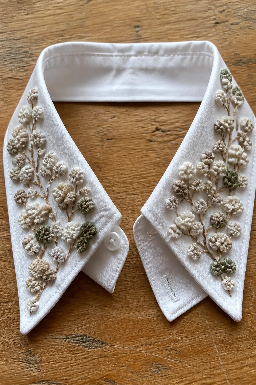 White shirt collar with beige and green floral embroidery on wooden surface.