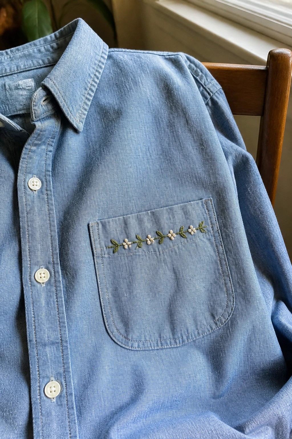 Light blue denim shirt with floral embroidery on pocket atop wooden chair