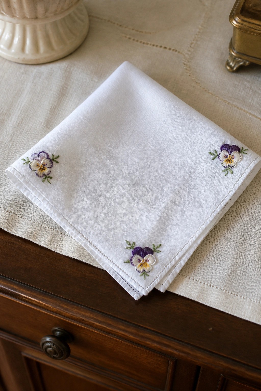 White handkerchief with purple and yellow pansy embroidery in corners on wood table
