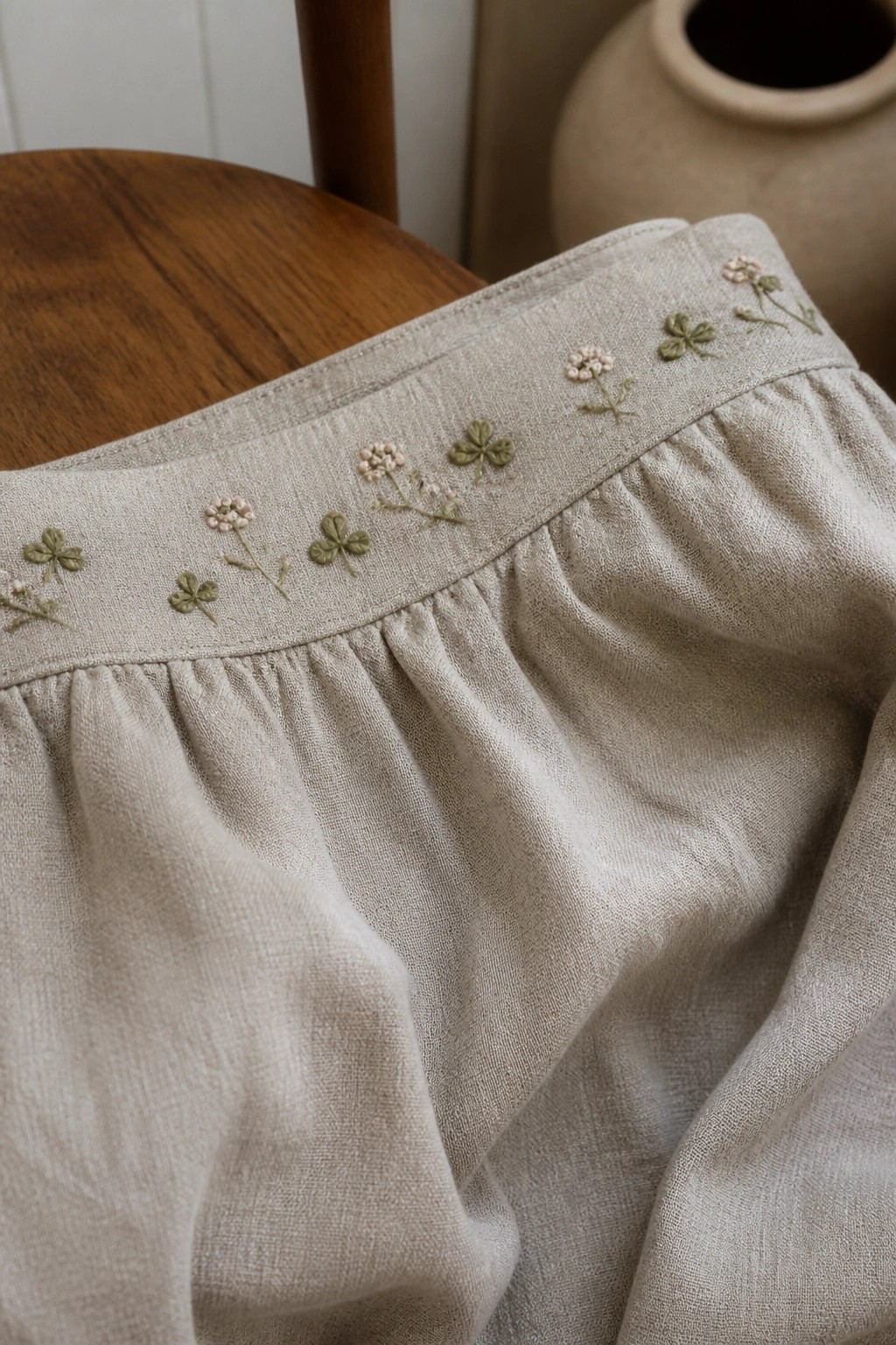 Beige linen skirt with delicate green clovers and pink floral embroidery on waistband.