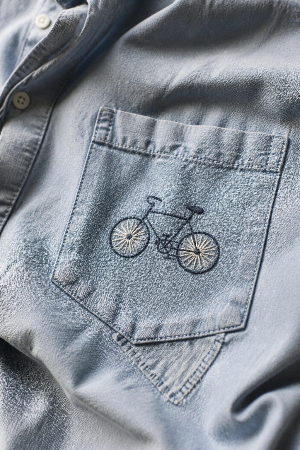 Light blue denim shirt with embroidered bicycle on chest pocket.