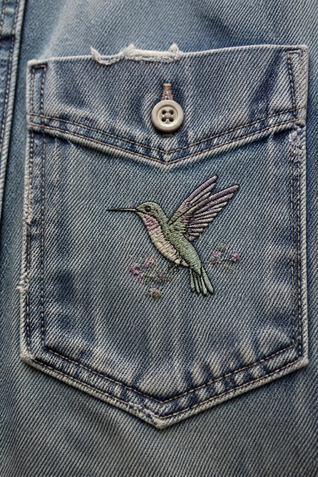Blue denim pocket with embroidered hummingbird, flowers, and button.