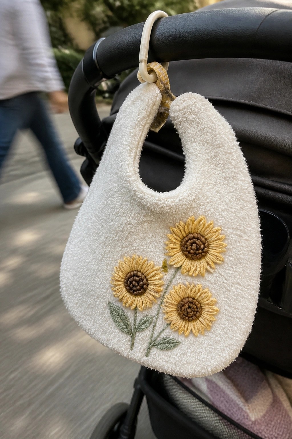 White terrycloth bib with embroidered sunflowers hanging from black stroller handle