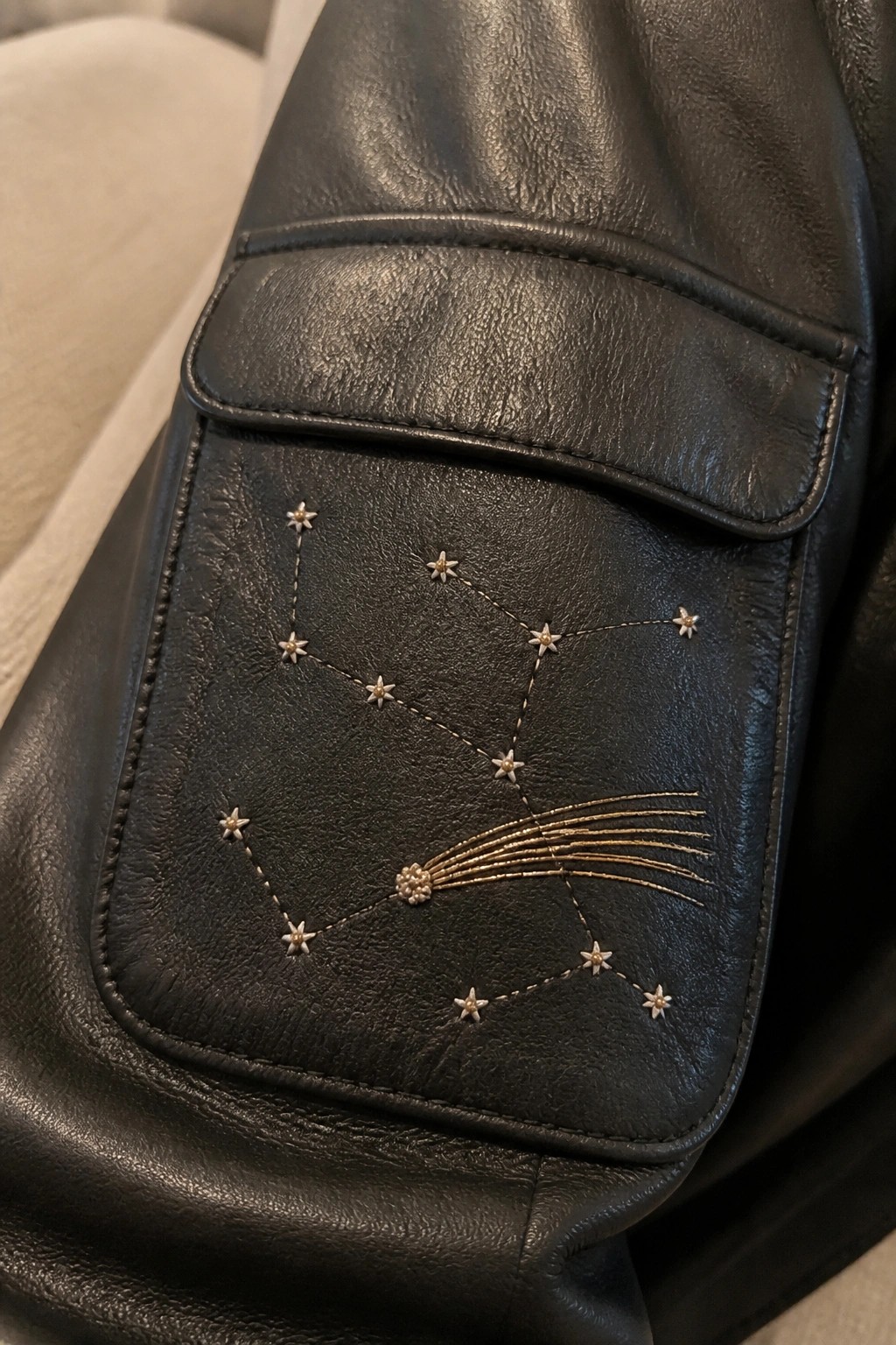 Black leather flap with embroidered constellation of gold stars and comet tail