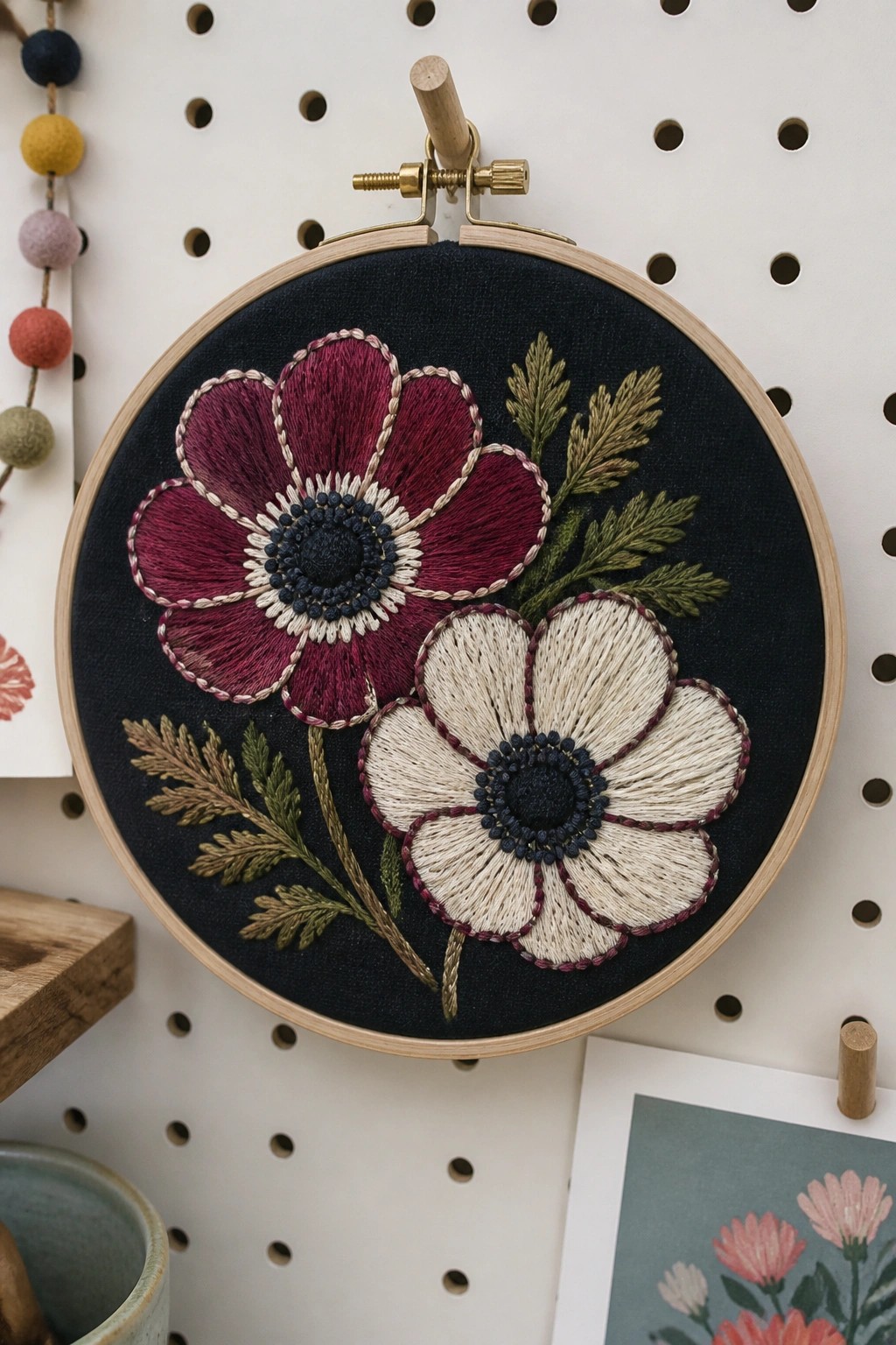 Maroon and cream flowers embroidered on dark fabric in a wooden hoop