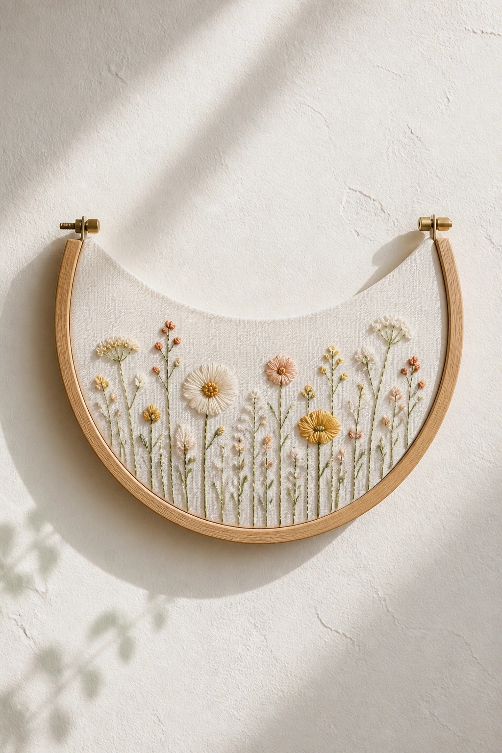Curved wooden hoop with delicate wildflower embroidery on white fabric against wall