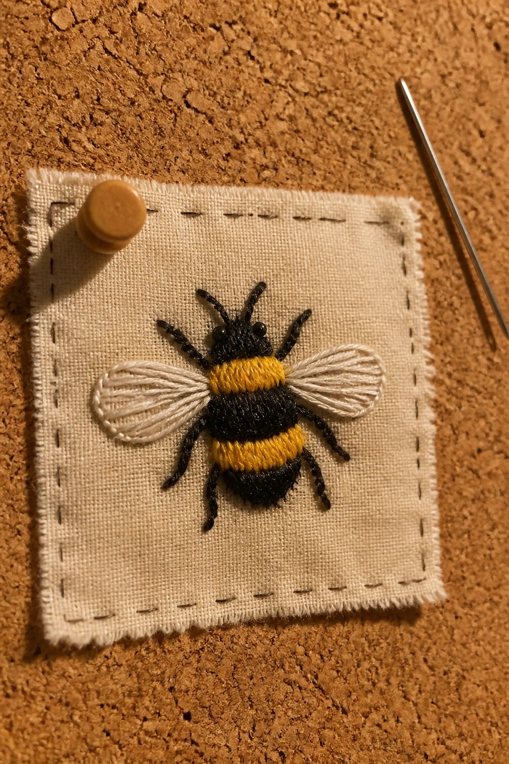 Embroidered bumblebee with black and yellow stripes on pinned fabric beside needle