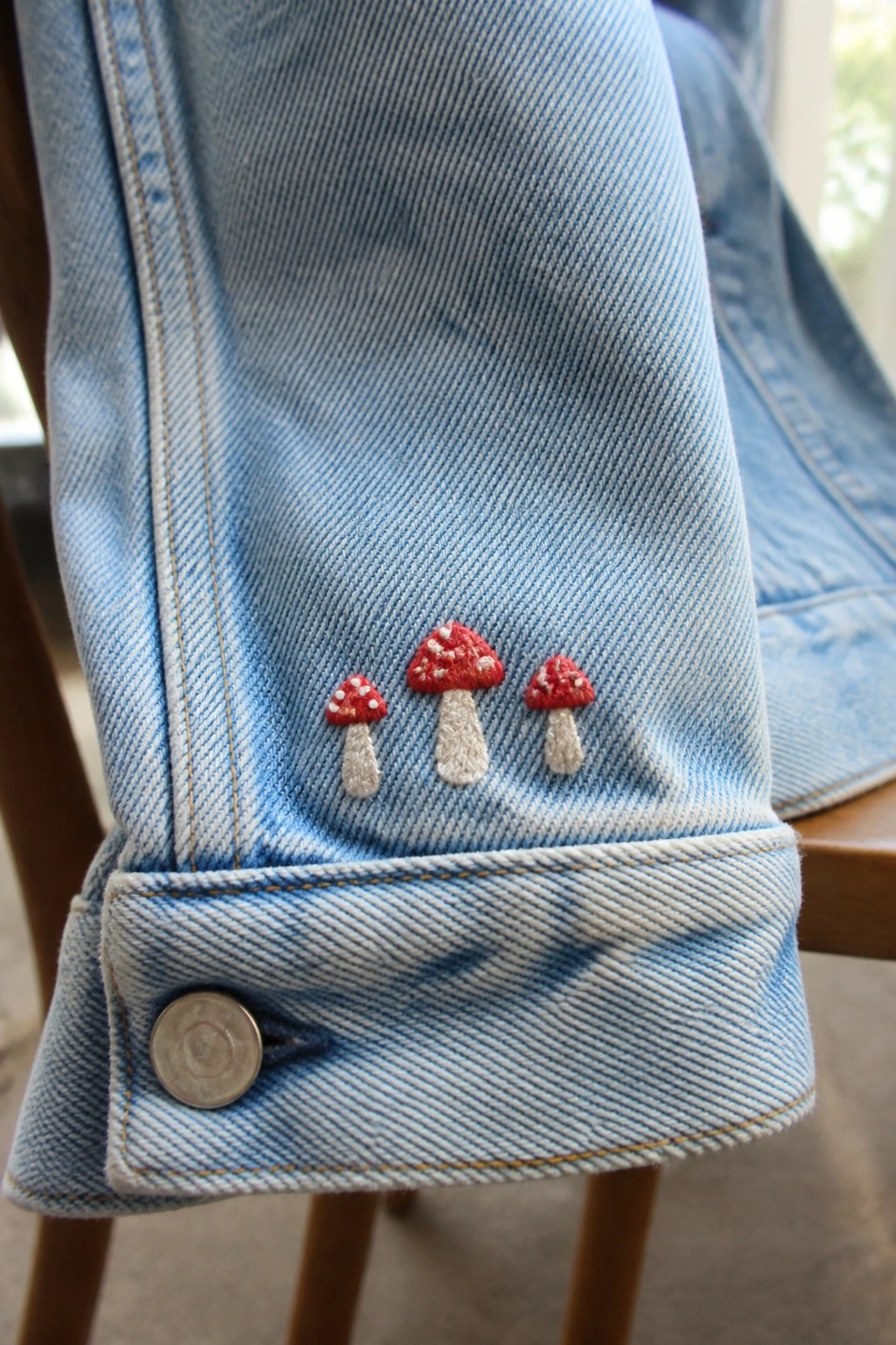 Light blue denim jacket cuff with three embroidered red mushrooms and button