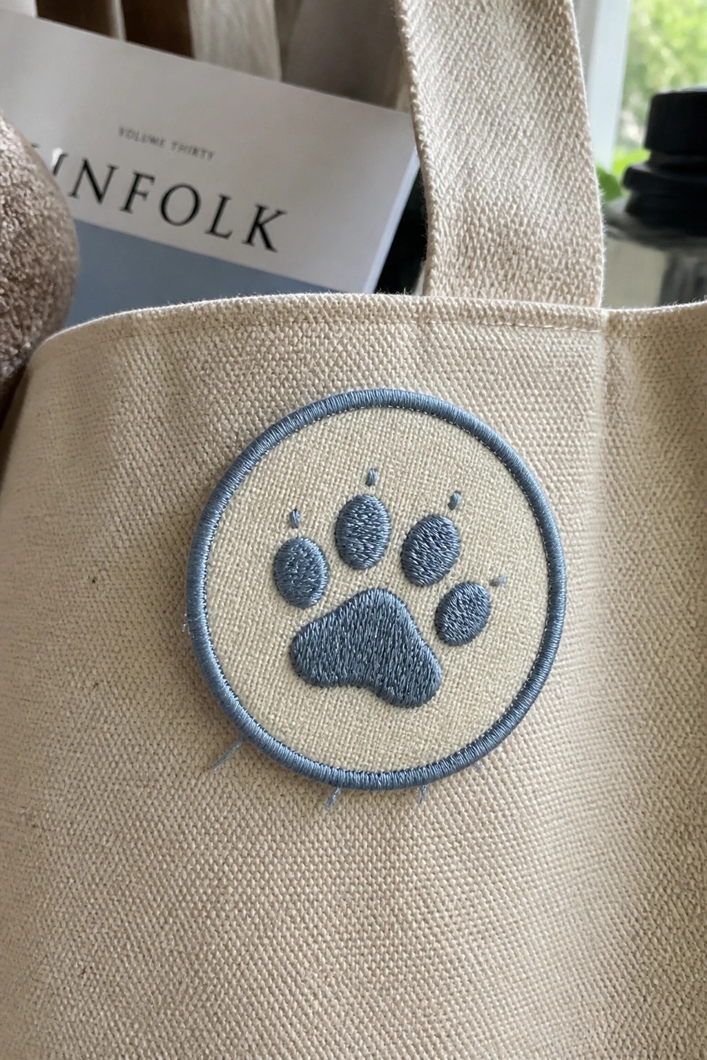 Beige canvas tote bag with blue embroidered paw print patch