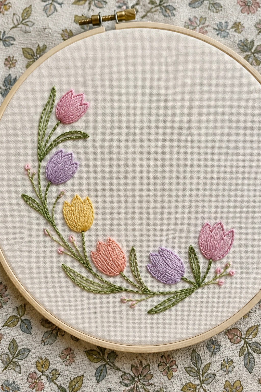 Wooden hoop with pastel embroidered tulips and green leaves on white fabric