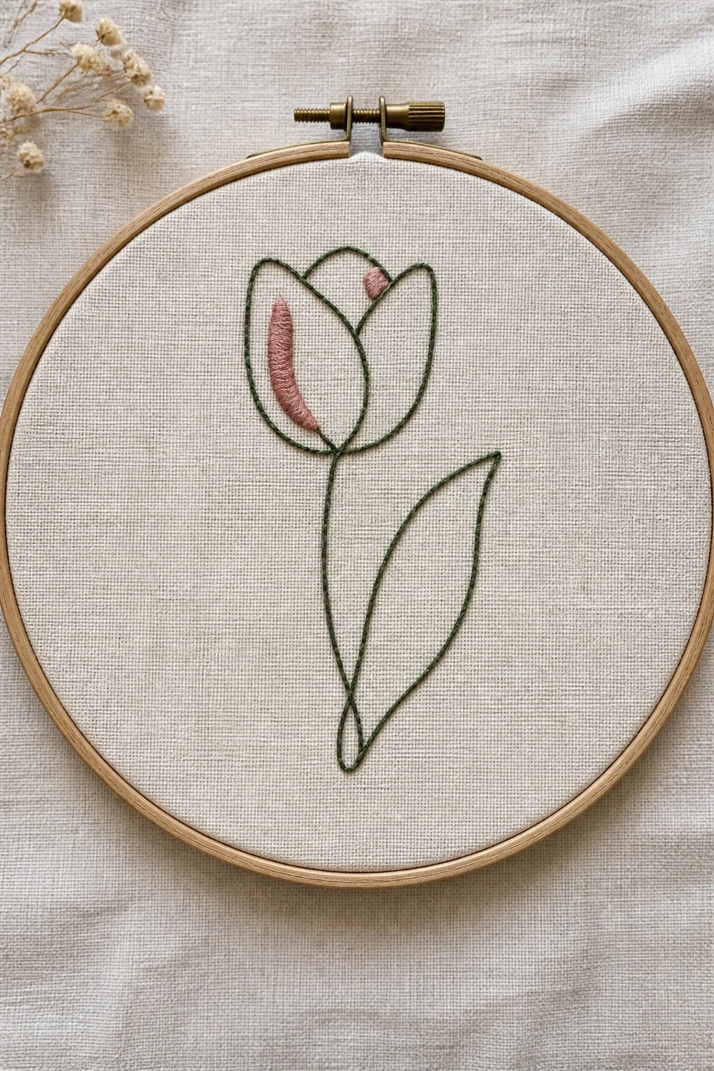 Wooden embroidery hoop with pink and green tulip stitched on beige fabric.