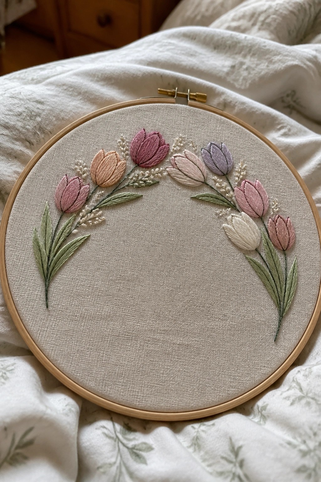 Wooden embroidery hoop with pastel tulips and green leaves on beige fabric