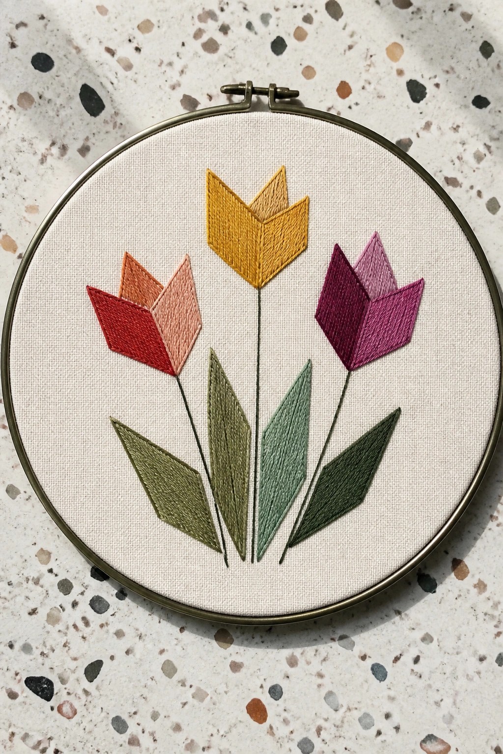 Circular embroidery hoop with three colorful tulips and green leaves on white fabric.