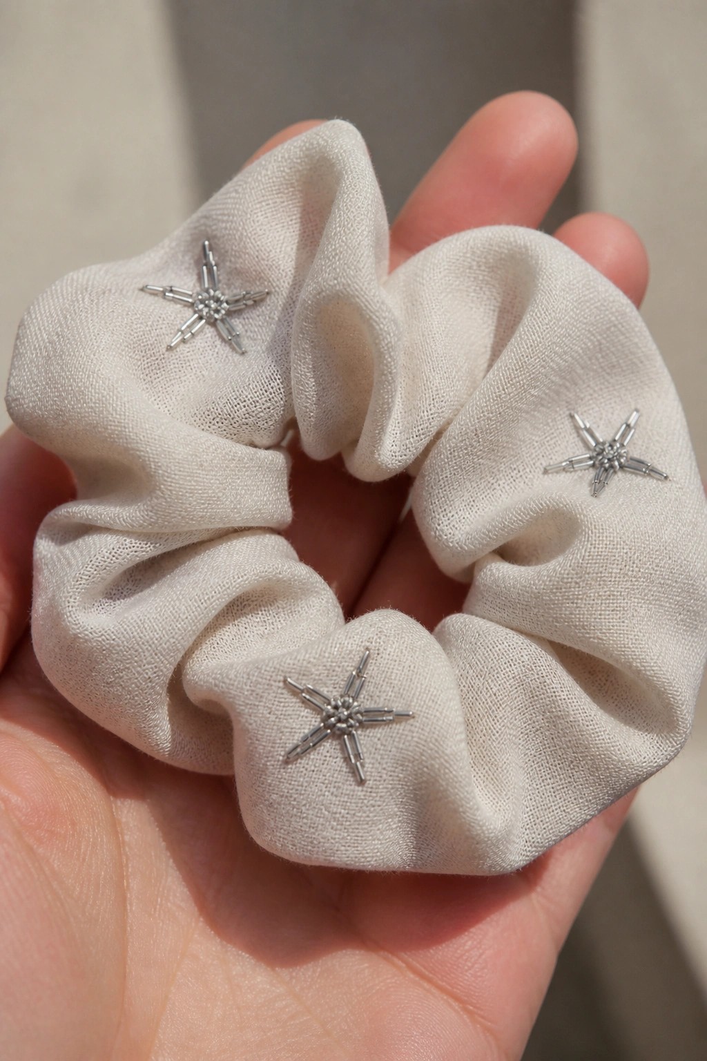 Hand holding cream scrunchie with three silver beaded star decorations.