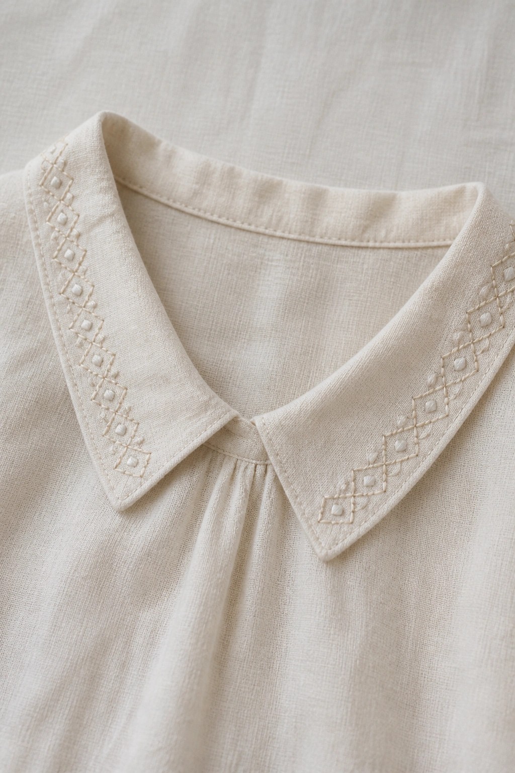 Cream linen blouse collar with geometric diamond embroidery along pointed edges