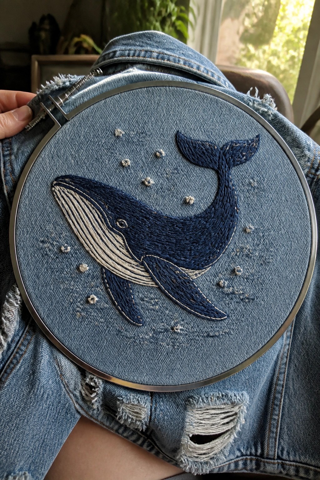 Ripped blue denim jacket with detailed whale embroidery in a metal hoop.