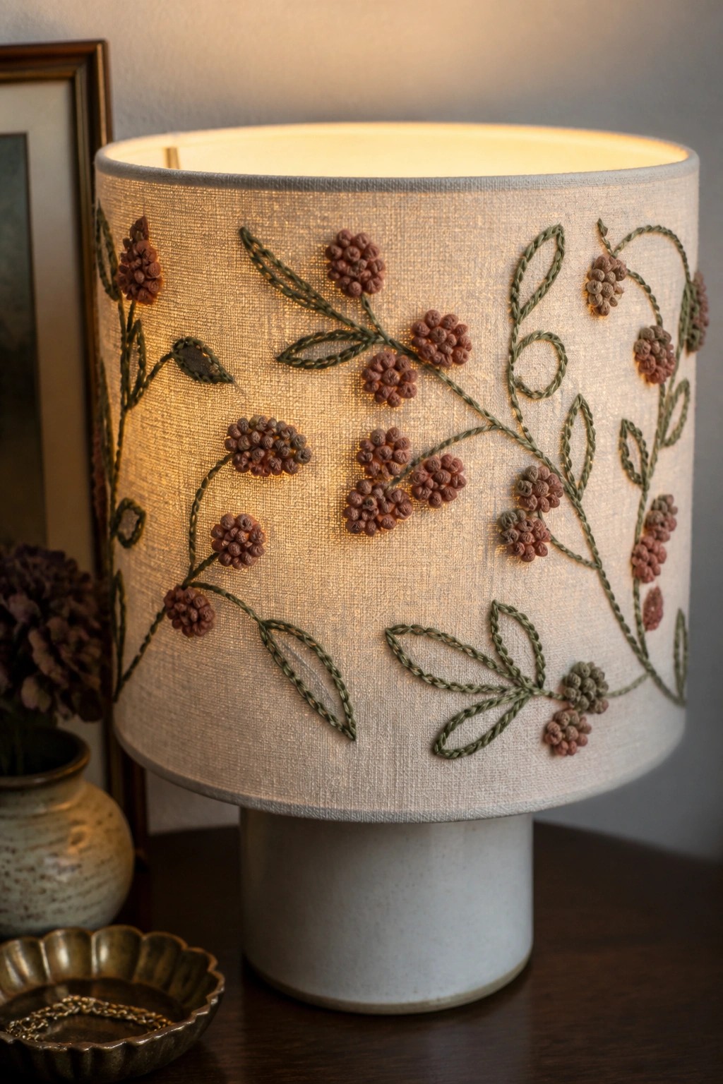 Glowing beige lampshade embroidered with green vines and brown floral clusters on ceramic base