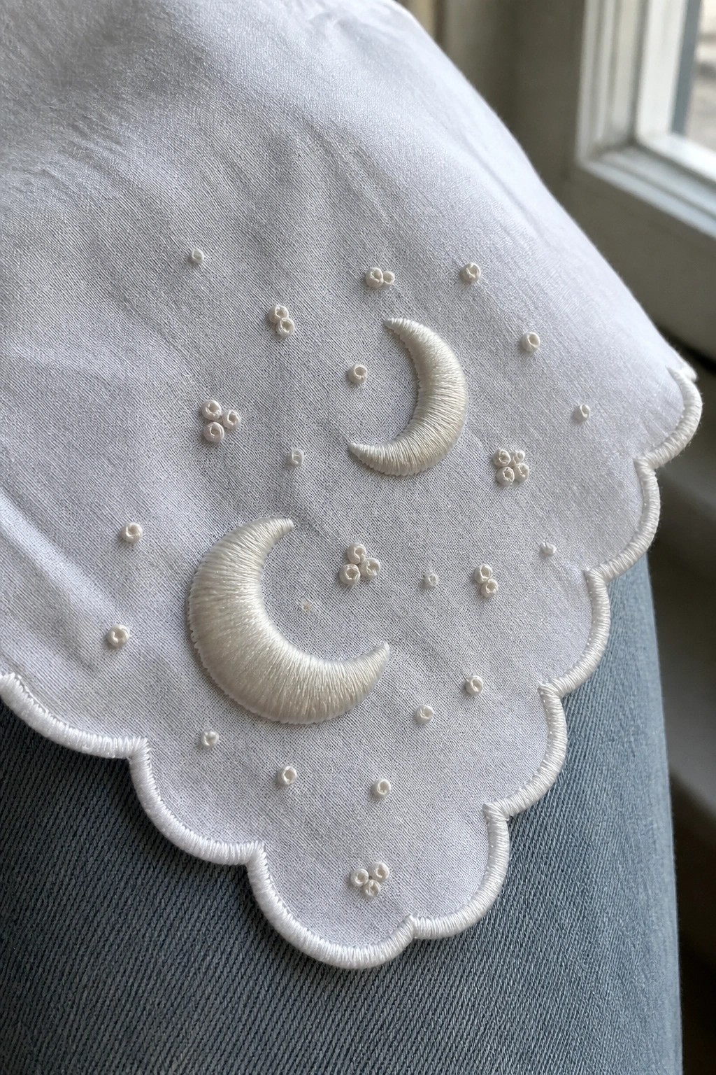 White scalloped fabric embroidered with two crescent moons and dotted patterns on denim.