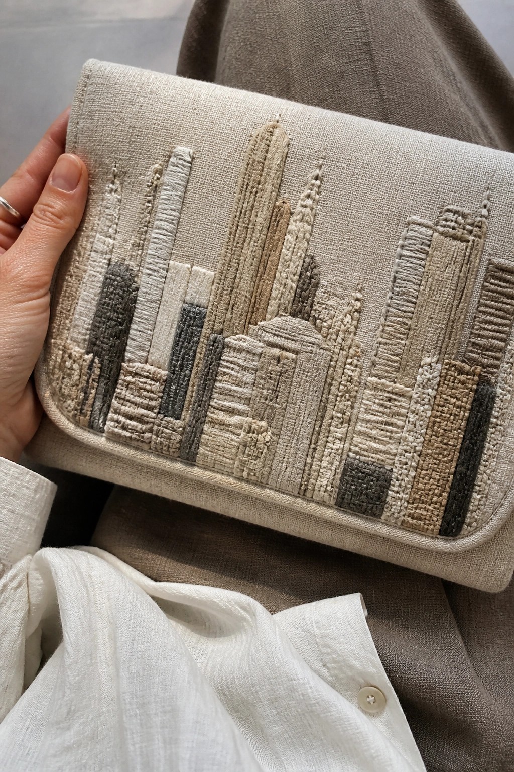 Close-up of a beige fabric clutch with a raised city skyline embroidered in neutral threads.