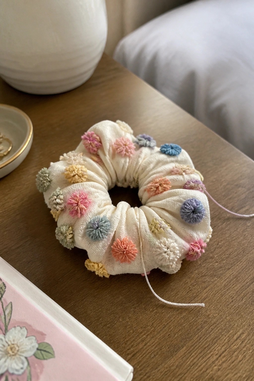 White scrunchie with pastel pom-poms on wooden table surface