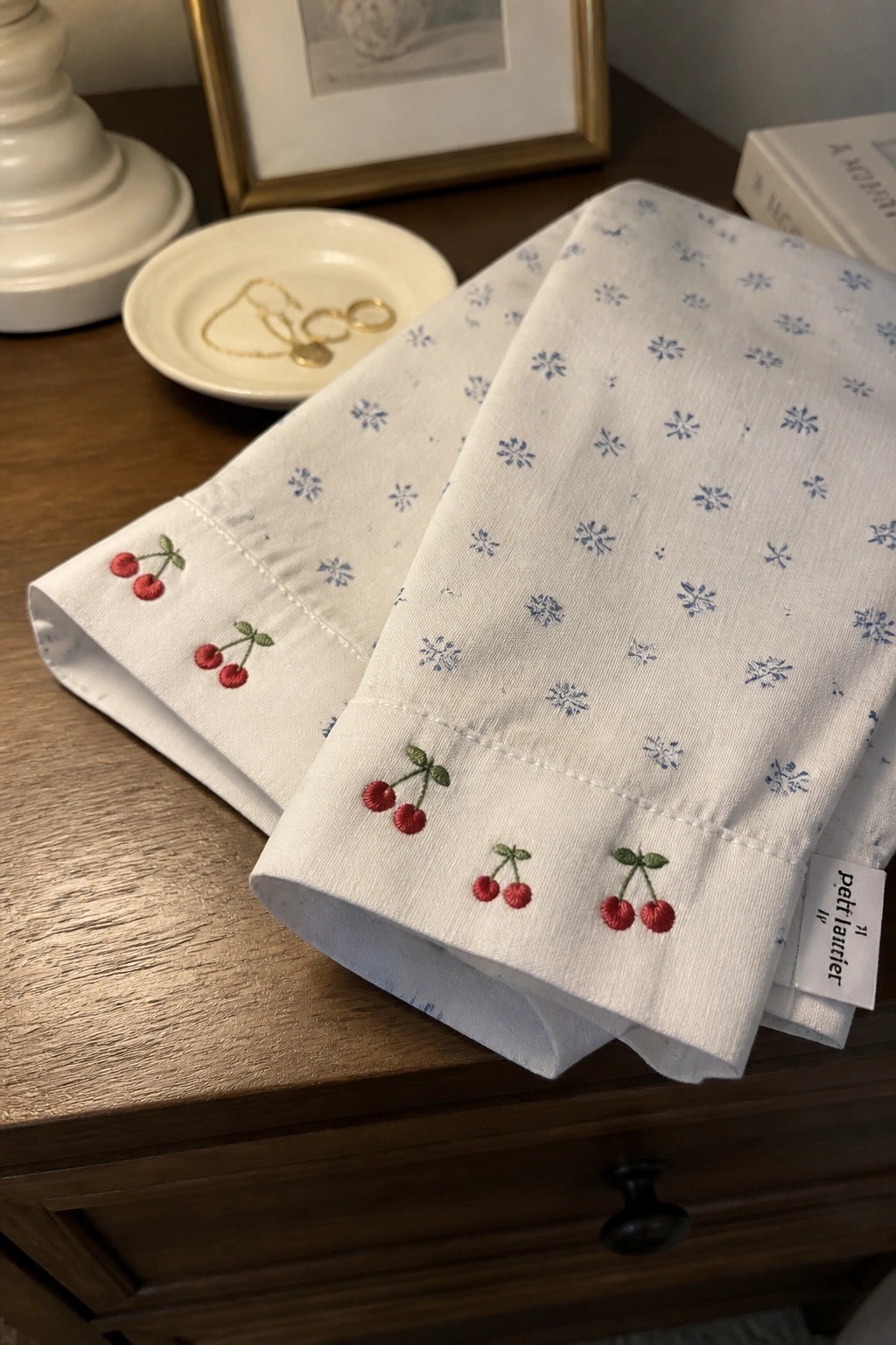 White fabric with blue snowflake print and red cherry embroidery stitched along the folded hems.