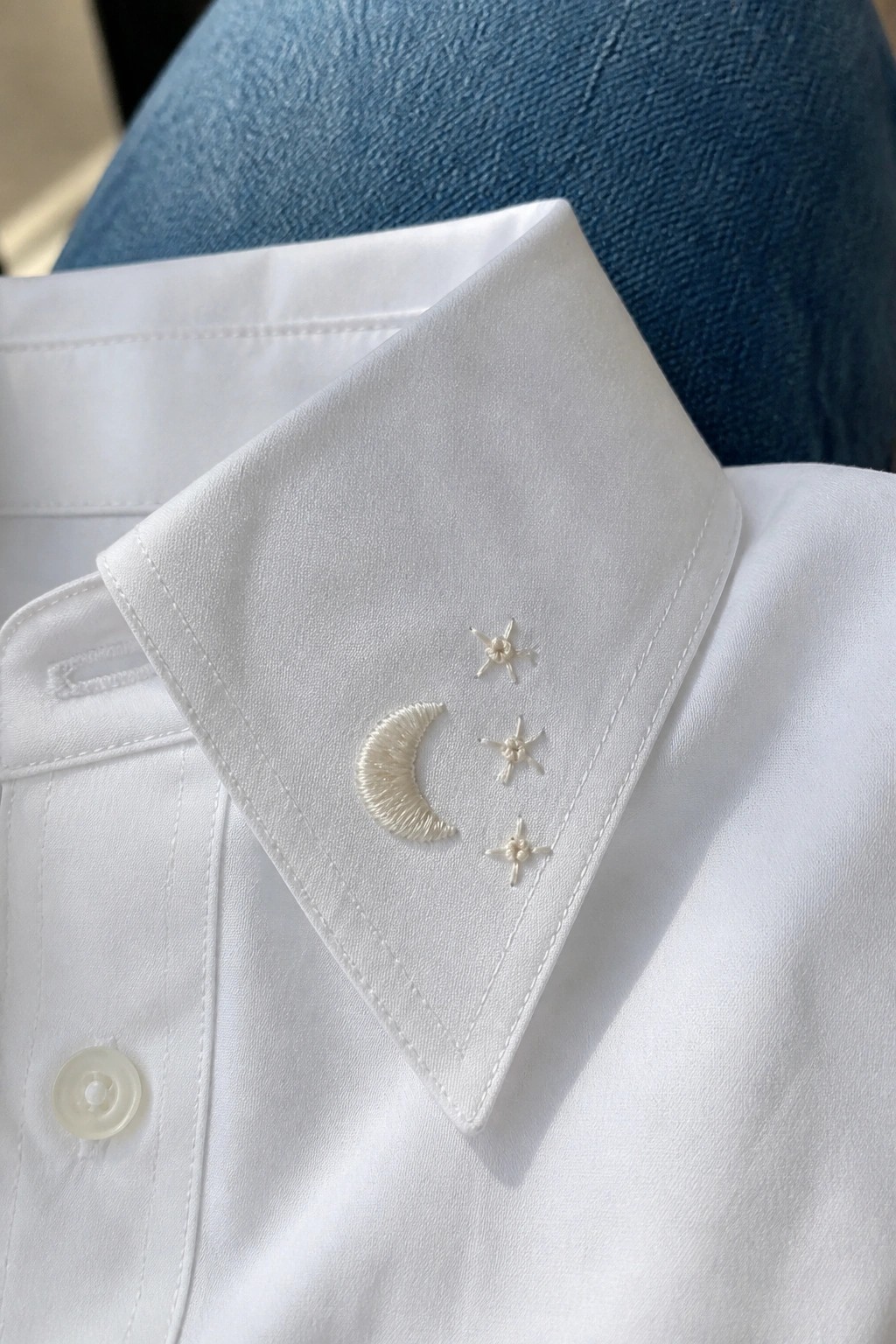 White shirt collar with embroidered crescent moon and three stars, blue jeans visible.
