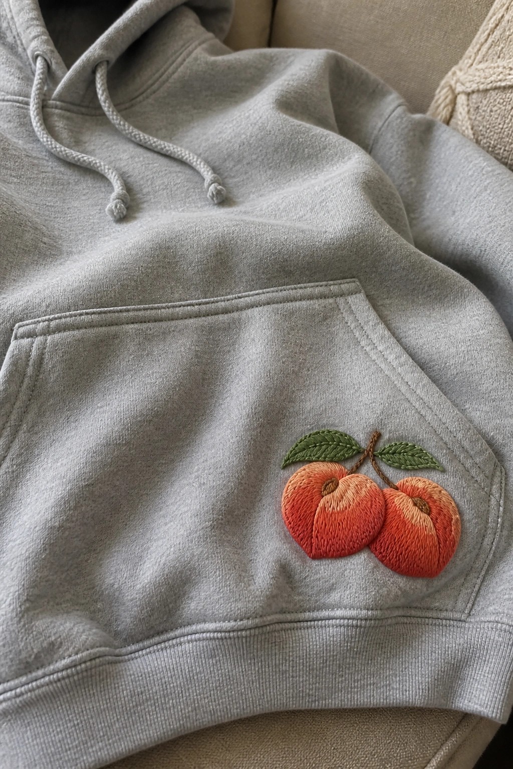 Gray hoodie pocket with embroidered orange peaches and green leaves