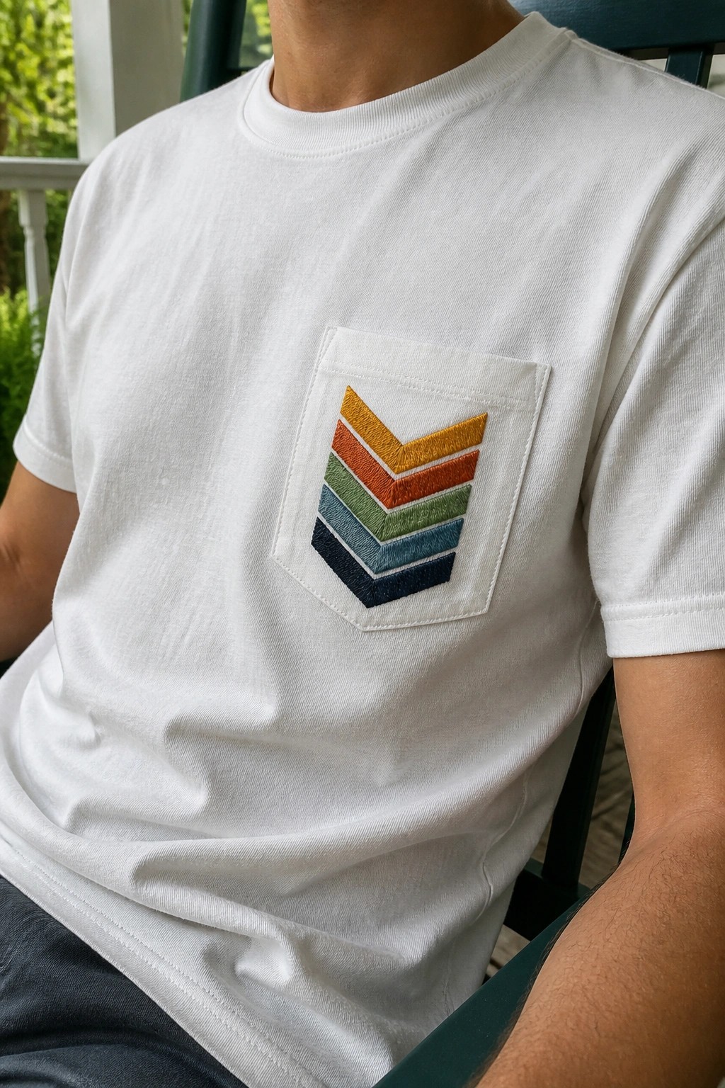 White t-shirt with chest pocket holding stacked embroidered chevrons in yellow, orange, green, blue, and navy.