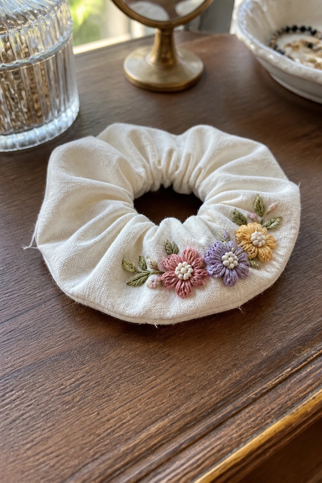 White scrunchie embroidered with pink, purple, and yellow flowers on wood