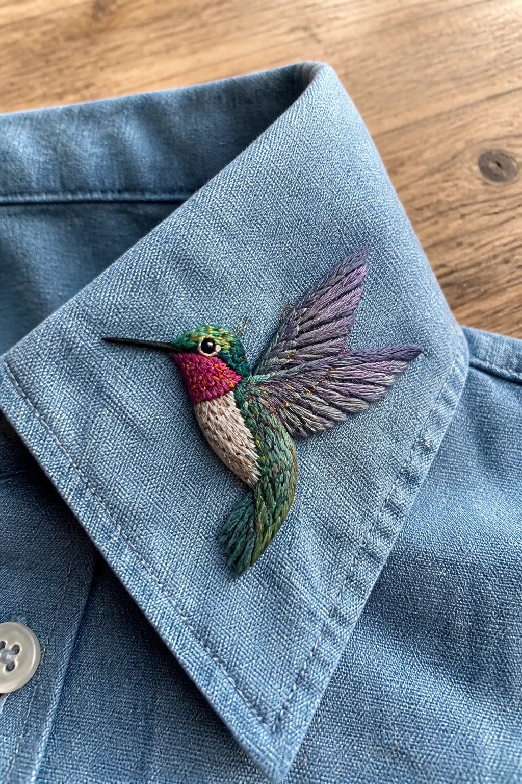 A colorful embroidered hummingbird on the collar of a blue denim shirt.