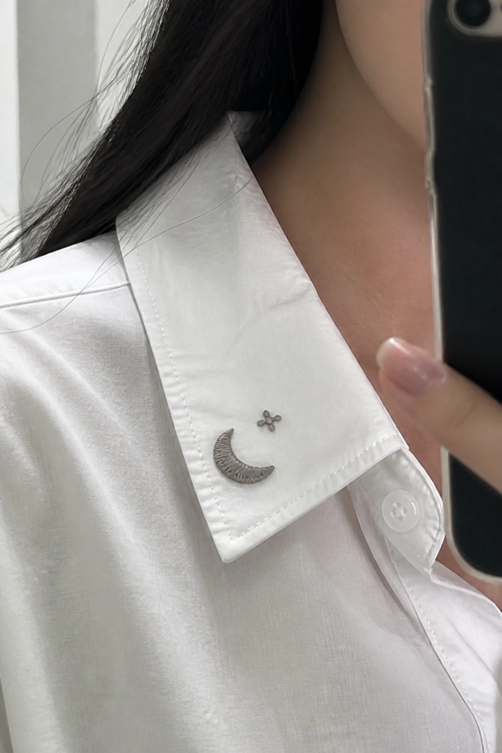 White shirt collar with silver crescent moon and flower pins on lapel.