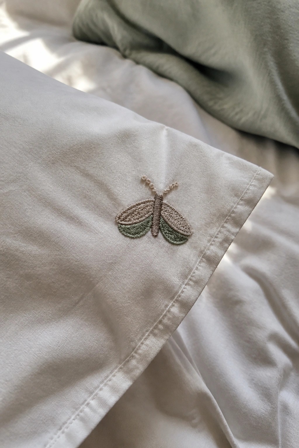 Small moth embroidered in beige and green thread near the edge of white fabric.