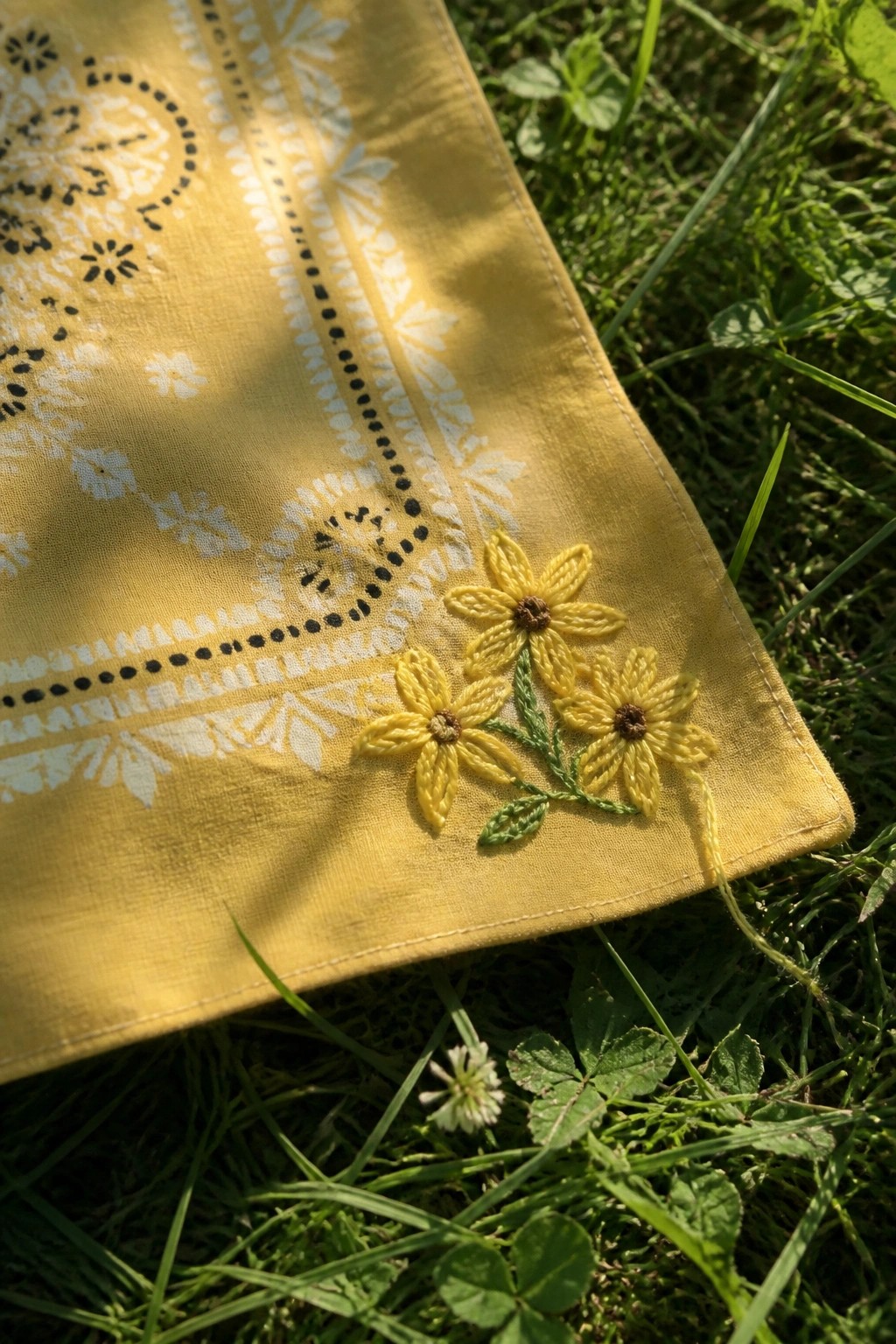 Yellow bandana with white patterns and yellow floral embroidery on green grass