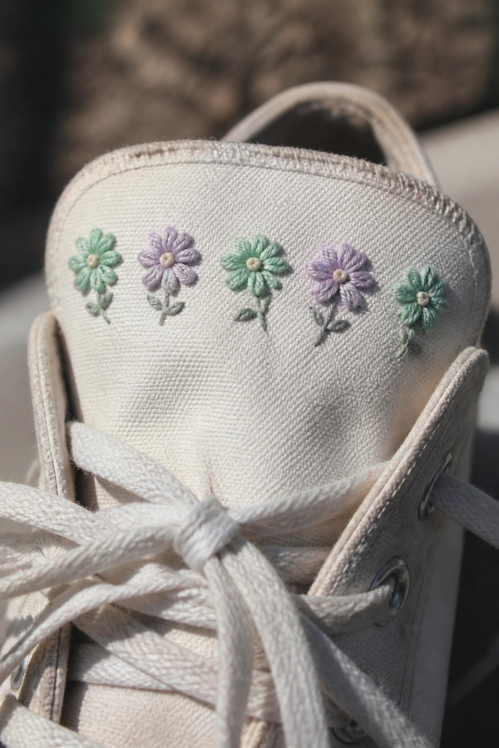 Close-up of off-white canvas sneaker with alternating lavender and mint embroidered flowers.