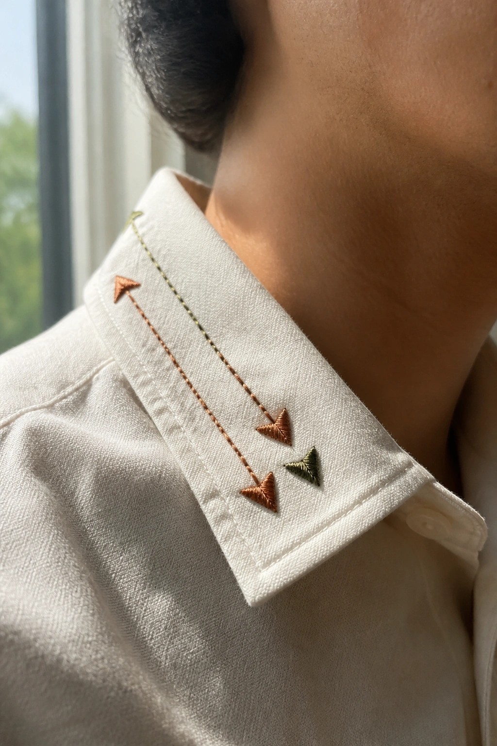 White shirt collar embroidered with orange and green downward arrows and dashed stitching.