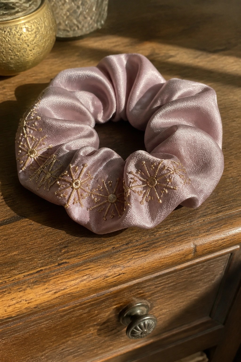 Pale pink satin scrunchie with gold star embroidery on wooden surface.