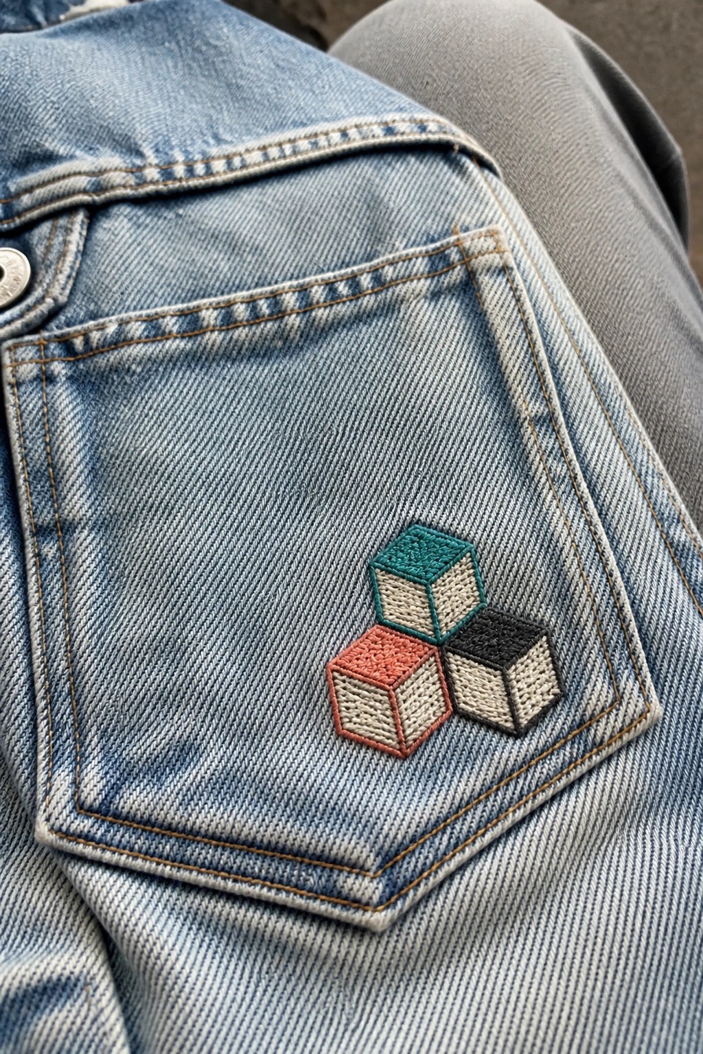 Blue denim pocket with embroidered teal, red, and black 3D cube patch