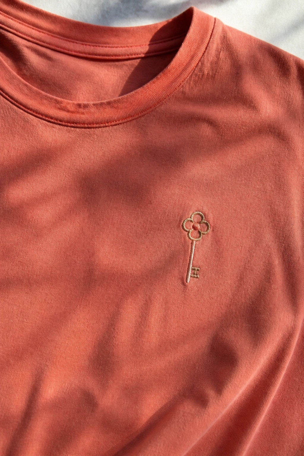 Close-up of a coral t-shirt with a small embroidered key on the left chest.