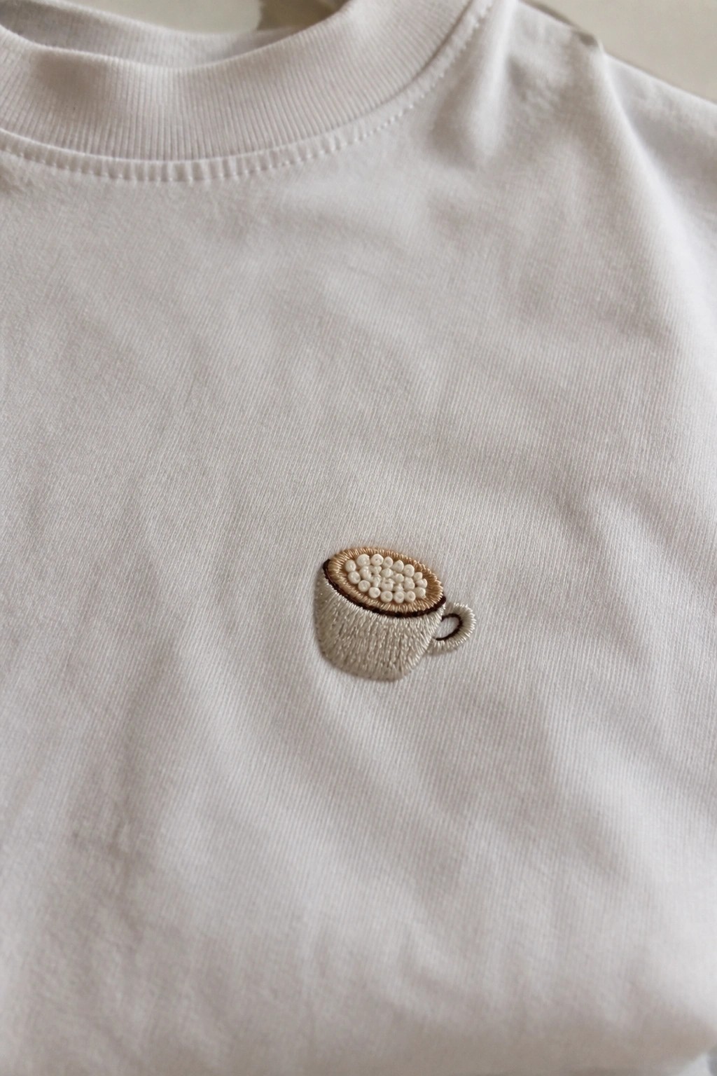 White t-shirt with embroidered beige coffee cup and white foam design
