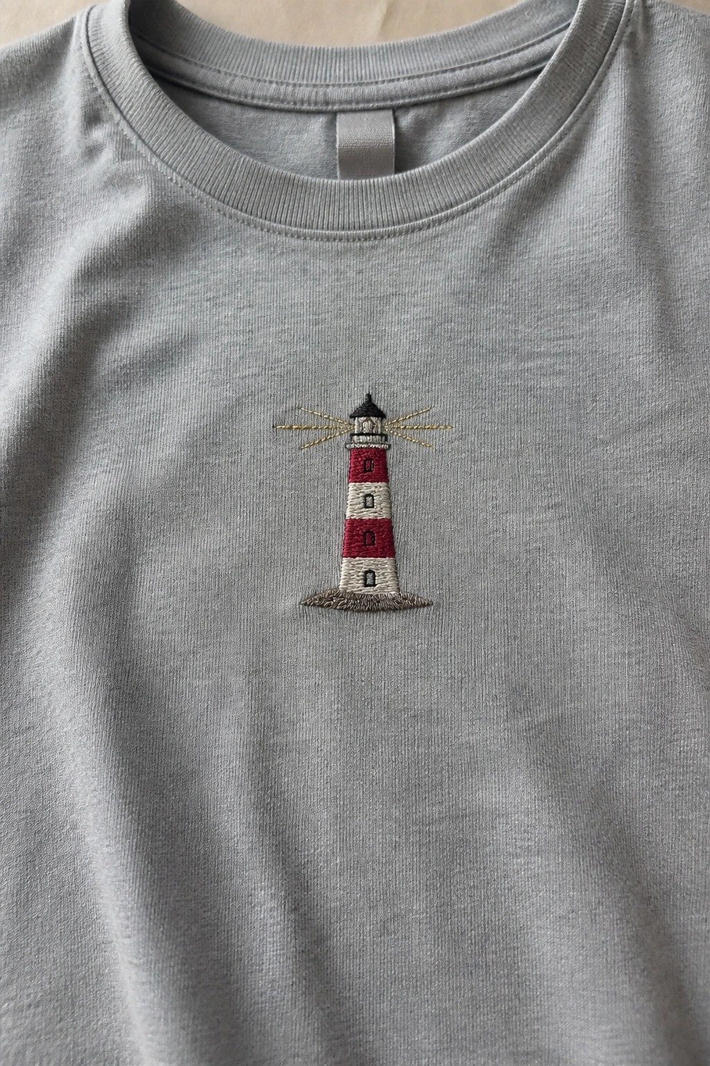 Gray t-shirt with embroidered red-and-white striped lighthouse and yellow light rays
