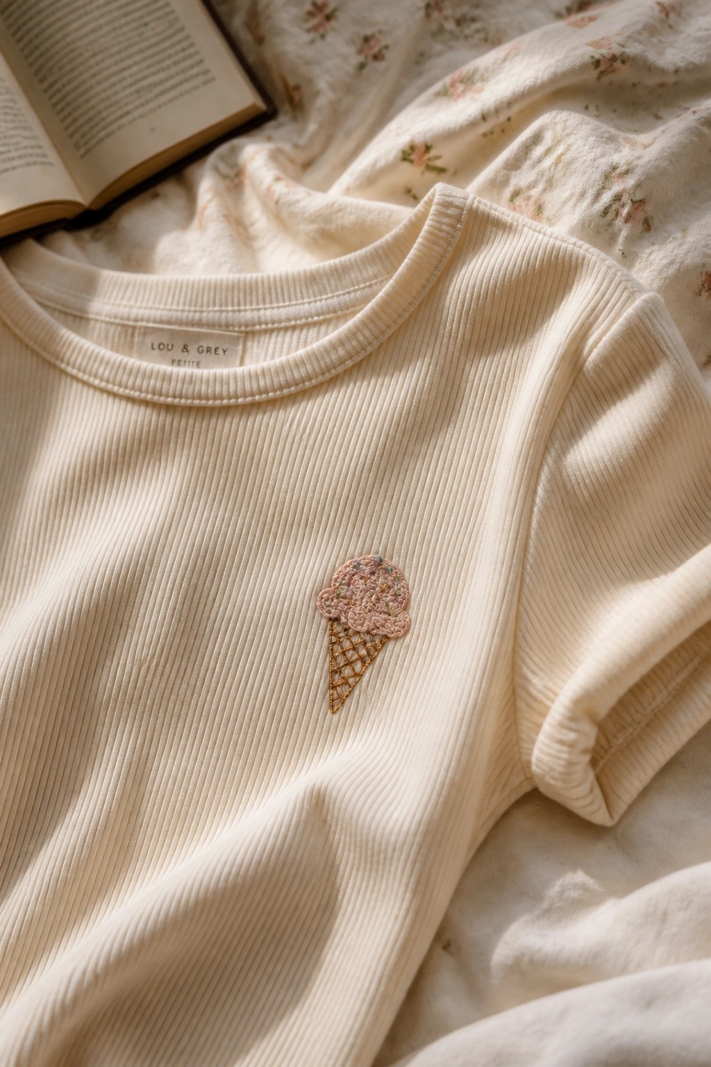 Cream ribbed shirt with ice cream embroidery beside open book on floral bedding