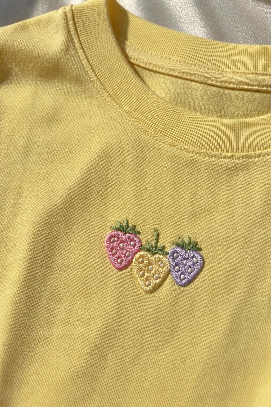 Yellow t-shirt with pink, yellow, and purple embroidered strawberries on the chest.