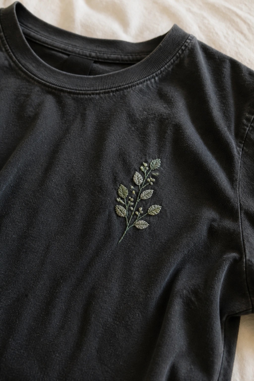 Black t-shirt with small embroidered green plant stem on the left chest.