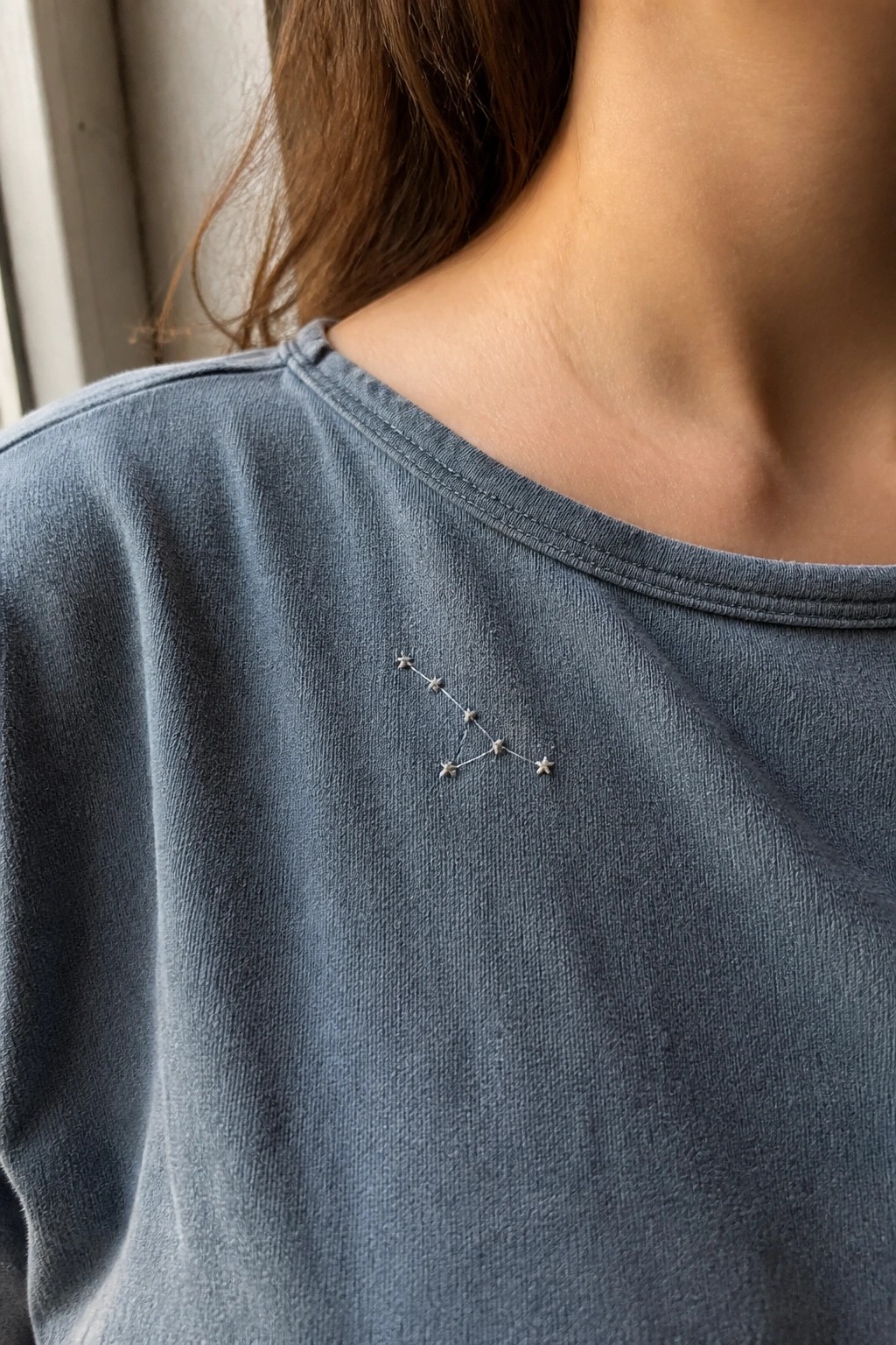 A blue t-shirt with a small embroidered constellation of connected stars on the left chest area.